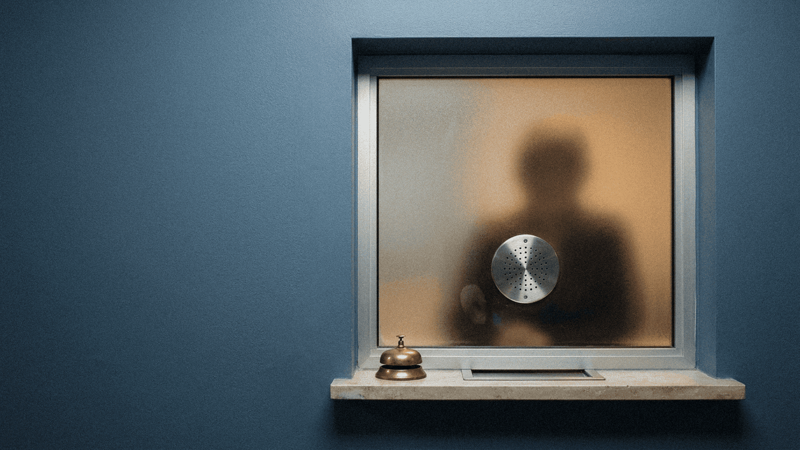 A round brushed-steel intercom grille lit from behind by a warm lamp, an ambiguous silhouette shadow visible through frosted glass, no resolvable face.