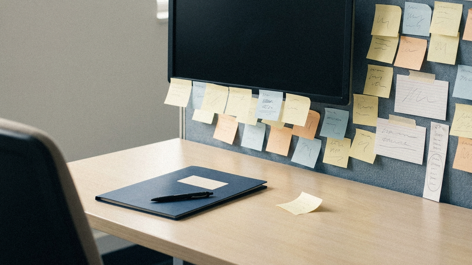 A cleared desk with a single thin navy folder resting on it, and behind it a wall crowded with sticky notes; no visible text.