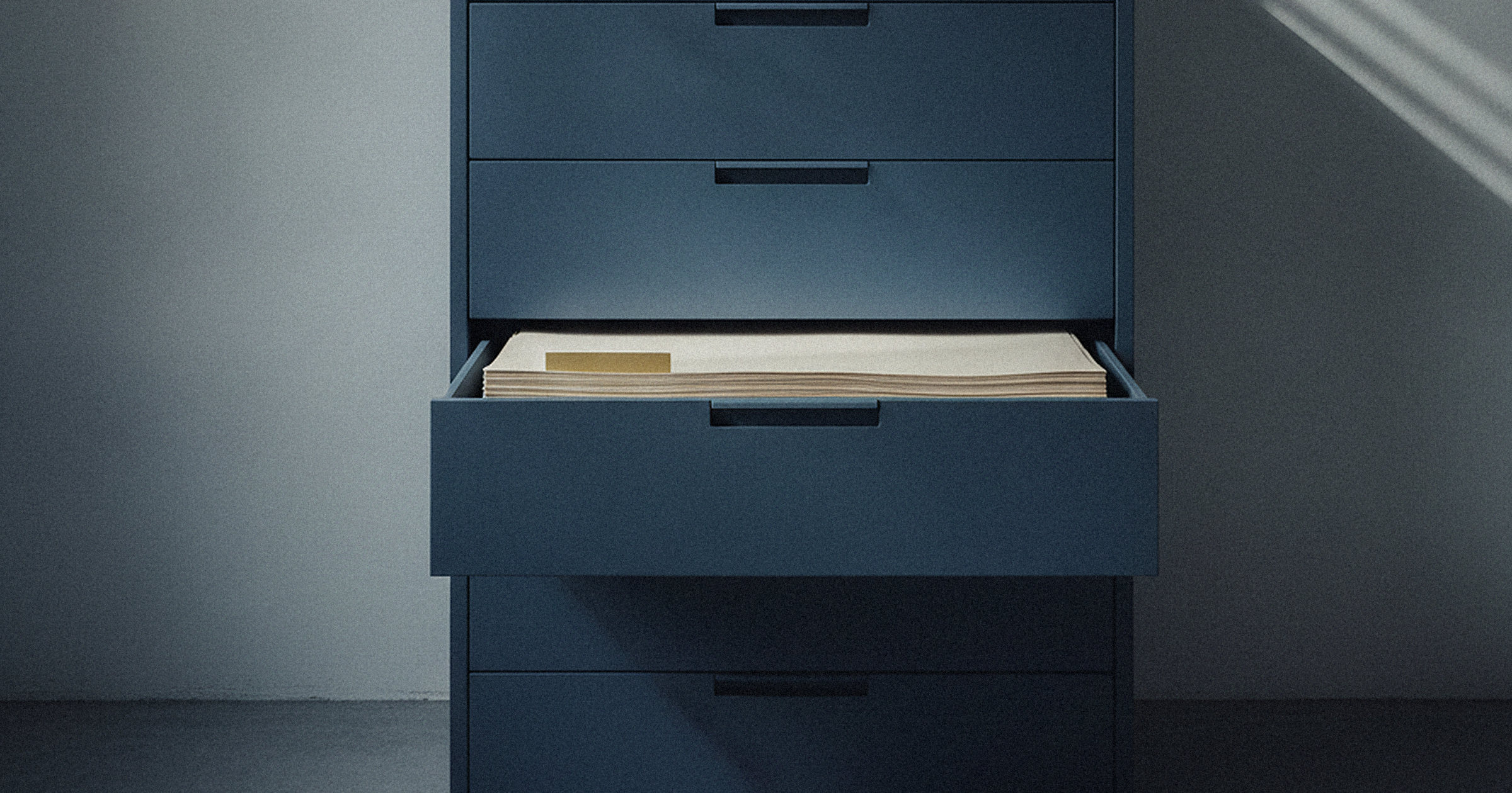 Deep blue five-drawer plan chest against a grey wall, one drawer pulled open and overfilled with a thick stack of pale paper, representing work an AI system left unresolved.
