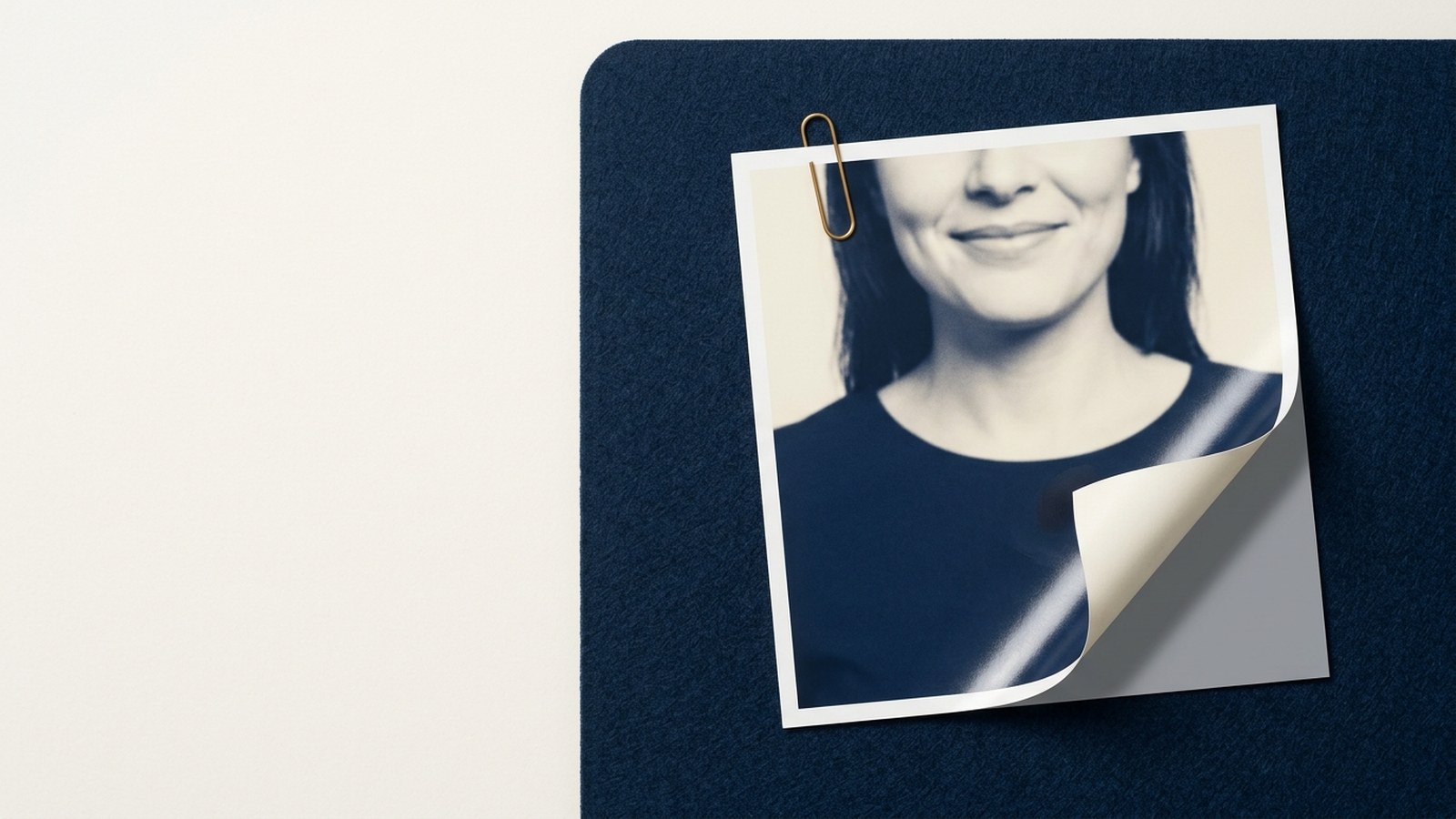 Editorial photograph-style still life on a warm paper desk: a printed portrait photograph with one corner peeled back to reveal a flat, blank grey layer beneath, in deep navy and paper tones with a single amber accent.