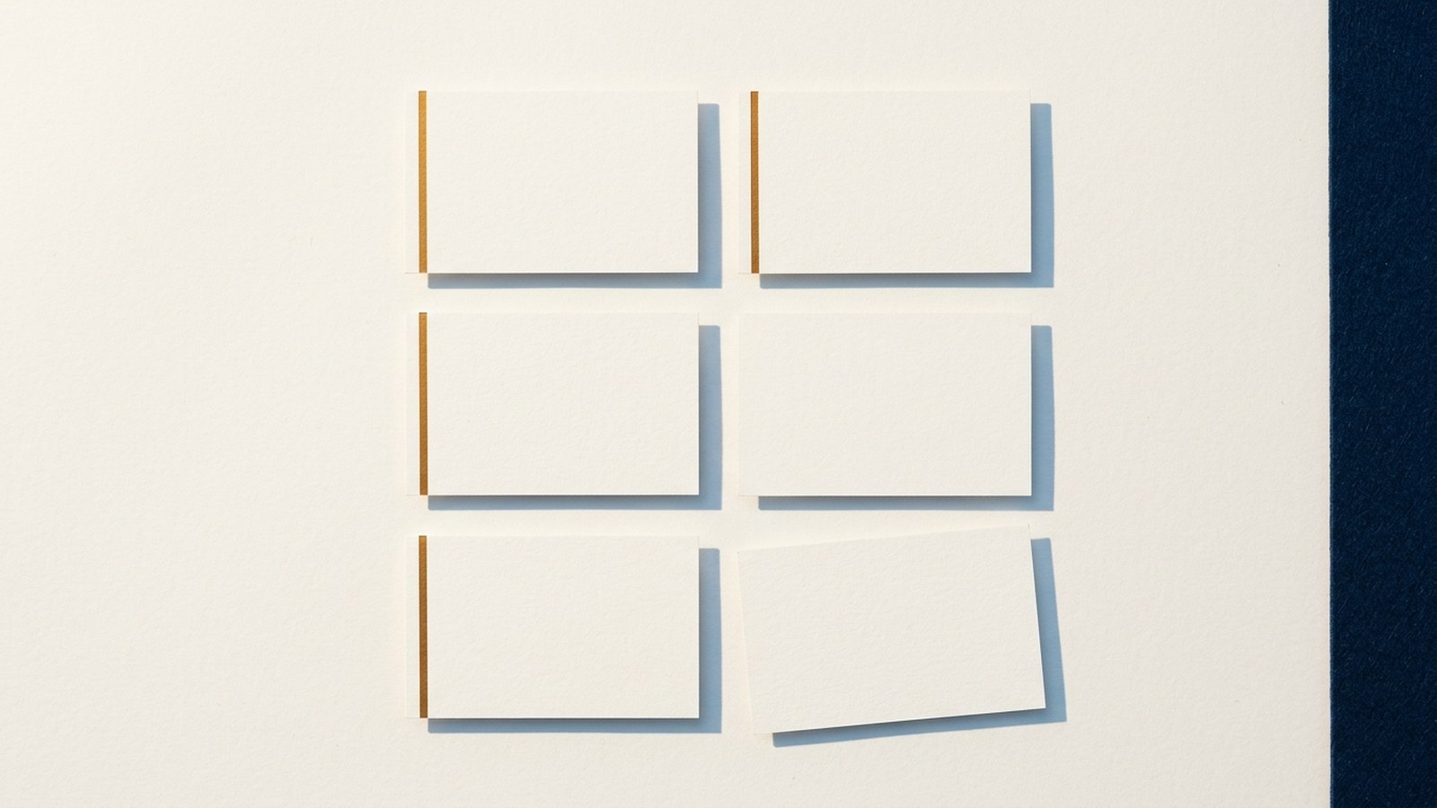 Editorial still life on a plain desk: six small paper cards laid out in two columns of three, four with a thin amber line along one edge and two left blank, soft daylight from the left and generous empty space around them.